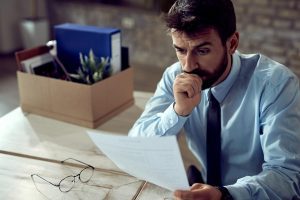 Susirūpinęs vyras peržiūri draudimo dokumentus, analizuodamas teisinę ir finansinę riziką.