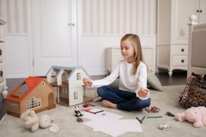 Gražiai suprojektuotas lėlių namelis su miniatiūriniais baldais ir figūrėlėmis vaiko žaidimų kambaryje.
